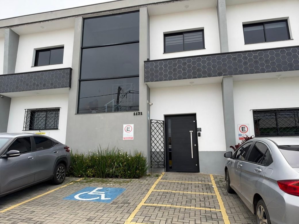 Fachada do prédio no número 1171 da Rua Frei Antônio de Pádua, com a porta de entrada preta e vagas na frente