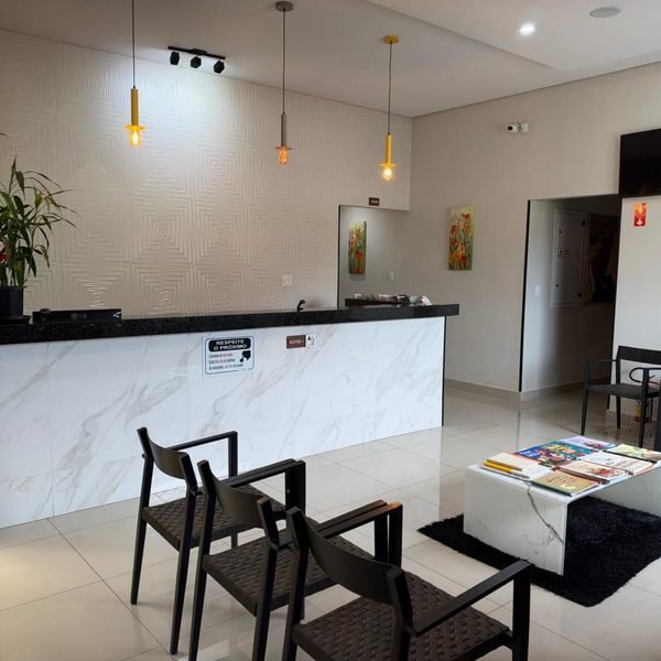 Recepção do prédio, com balcão de tampo de granito preto e frente branca, cadeiras e mesa de centro com livros