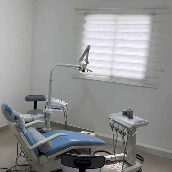 Sala de atendimento da Dra. Paula, clara, com cadeira azul e janela com persiana