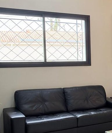 Sala de espera do prédio, com sofá de couro preto e janela ampla com grade branca